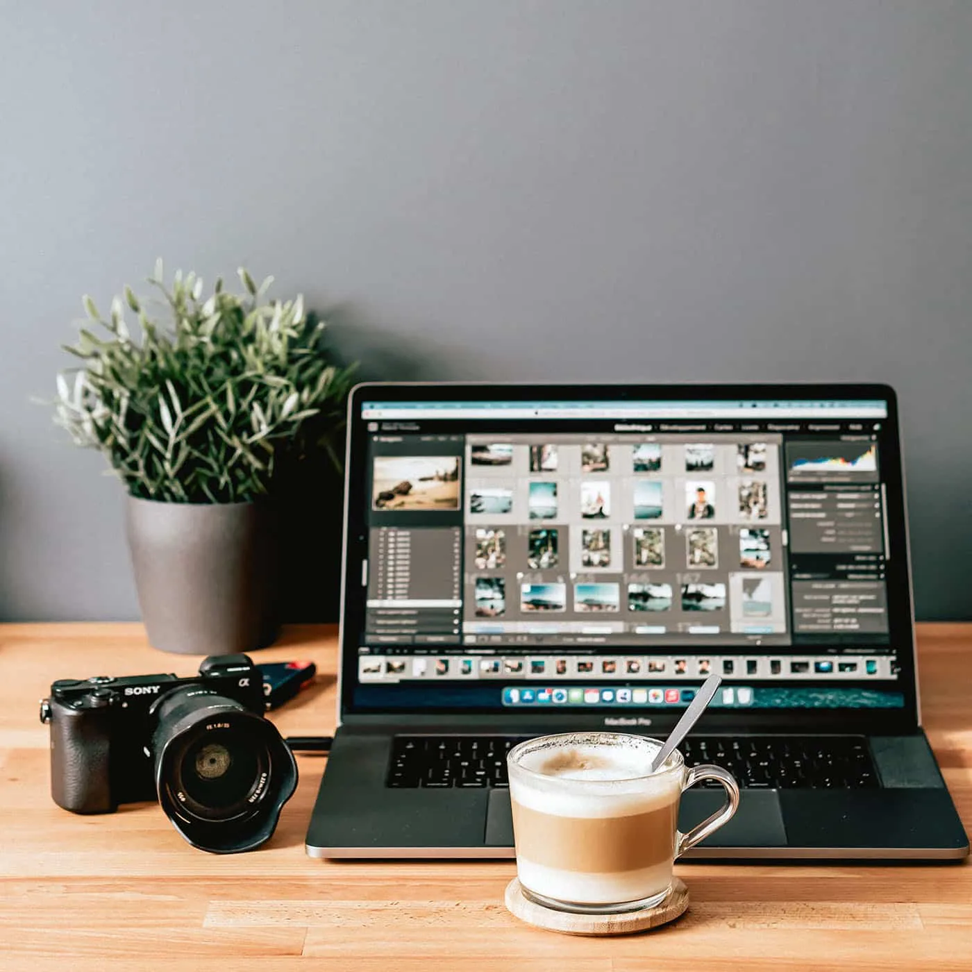 Behind the Scenes: Photo Editing Mastery at UA-Visions Professional photo editing workspace with a laptop displaying photo management software, a Sony camera, and a cup of coffee on a wooden desk.