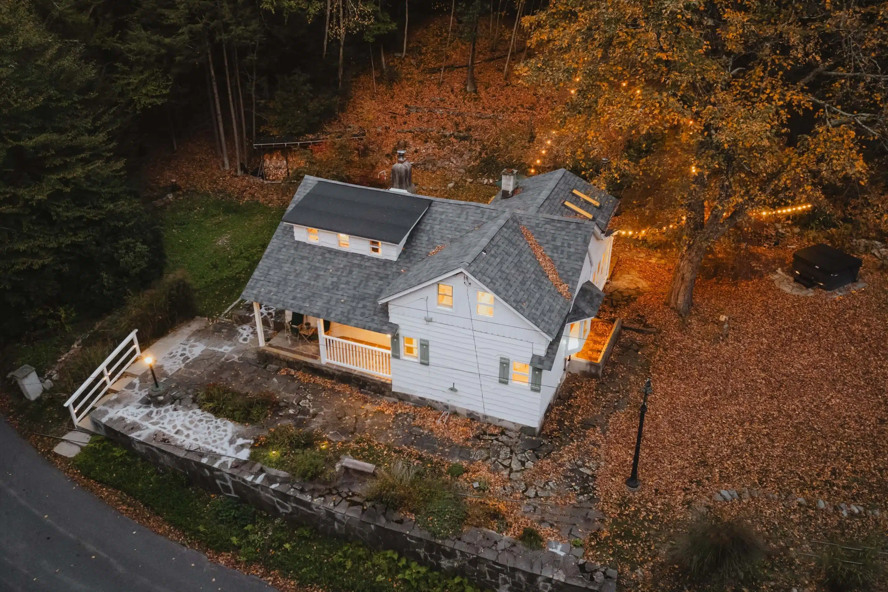 Autumn Serenity: Aerial View of a Cozy Home Aerial view of a picturesque house in autumn with a cozy fire pit and a solitary figure enjoying the tranquil evening.